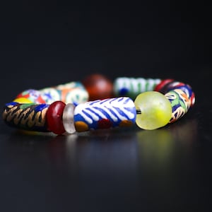 Pode incluir: Um bracelete de contas coloridas com uma variedade de padrões e cores, incluindo azul, vermelho, amarelo, verde e branco.