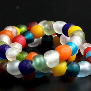 May include: A colourful bracelet made of glass beads in various shapes and sizes. The beads are arranged in a random pattern and include shades of blue, green, red, orange, yellow, and white.