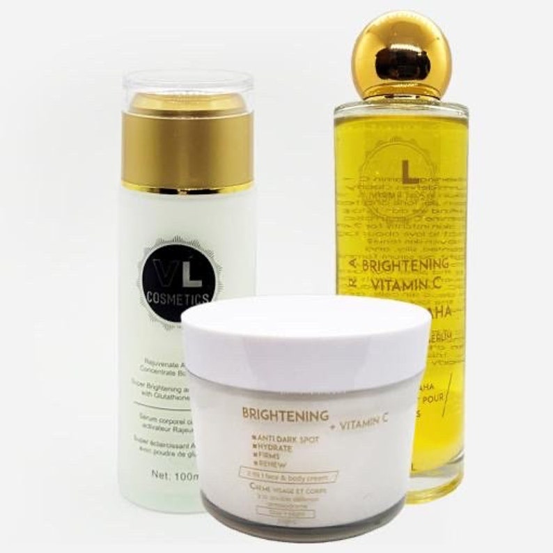 May include: Three skincare products in gold and white packaging. A serum bottle with a gold lid and label that reads "VL Cosmetics". A jar of face and body cream with the text "Brightening Anti-Dark Spot Hydrate Firms Renew Creme Visage et Corps". A glass bottle of oil with a gold lid and label that reads "Brightening Vitamin C".