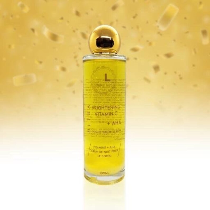 May include: A clear glass bottle with a gold lid and label. The label reads "L Brightening Vitamin C + AHA 3-Night Body Serum Vitamine + AHA Serum de Nuit Pour Le Corps 100ML".