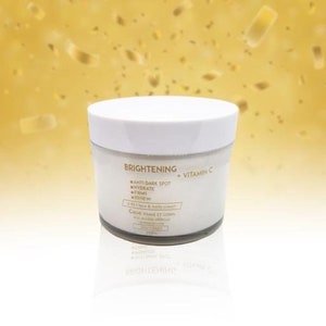 May include: White jar of brightening face and body cream with gold lettering that reads "BRIGHTENING + VITAMIN C" and lists the benefits: "ANTI DARK SPOT, HYDRATE, FIRMS, RENEW".