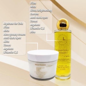 May include: Two bottles of skin care products. The bottle on the left is a white jar with a gold label that says "Brightening Anti-Dark Spot Vitamin C". The bottle on the right is a clear glass bottle with a gold cap and a gold label that says "Brightening Vitamin C + AHA Night Body Serum".