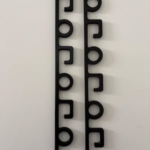 Puede incluir: Dos piezas de arte mural verticales negras que deletrean la palabra "POP" en una fuente estilizada. Las letras están conectadas por líneas rectas y tienen un diseño moderno y minimalista. Las piezas están montadas en una pared blanca.