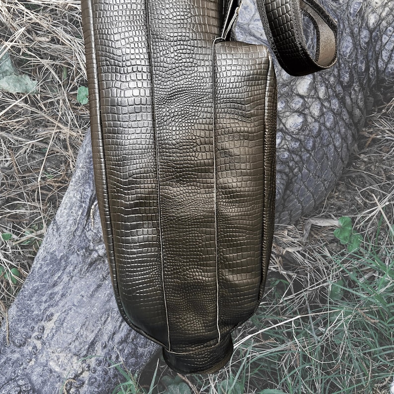Pu&ograve; includere: Una borsa da golf in pelle marrone con un motivo a coccodrillo in rilievo. La borsa ha una tracolla e una chiusura a zip.