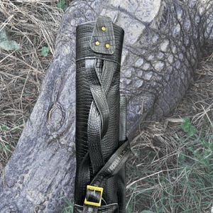 Pu&ograve; includere: Borsa da golf in pelle nera con motivo coccodrilo e dettagli dorati. La borsa ha una chiusura a fibbia e una cerniera.
