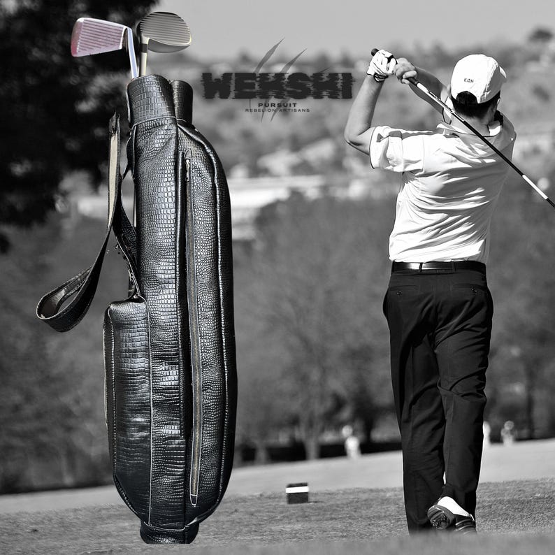 Pu&ograve; includere: Una sacca da golf in pelle nera con una tasca con cerniera e una tracolla. La sacca &egrave; in piedi su un campo erboso verde. Un golfista sta swingando una mazza da golf sullo sfondo.