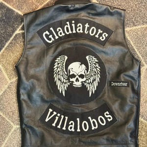 Puede incluir: Chaleco de cuero negro con parches. Los parches muestran las palabras "Gladiators" y "Villalobos" en blanco. Un parche central presenta una calavera con alas. También es visible la palabra "Downriver".