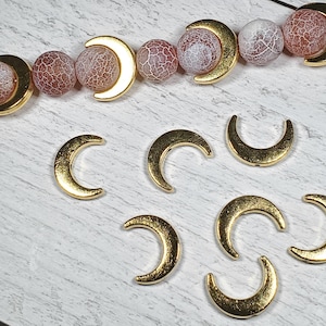 Puede incluir: Componentes para la fabricaci&oacute;n de joyas: abalorios dorados en forma de media luna y una hebra de cuentas redondas estampadas en rojo, rosa y blanco. Las cuentas tienen un patr&oacute;n agrietado en forma de telara&ntilde;a.