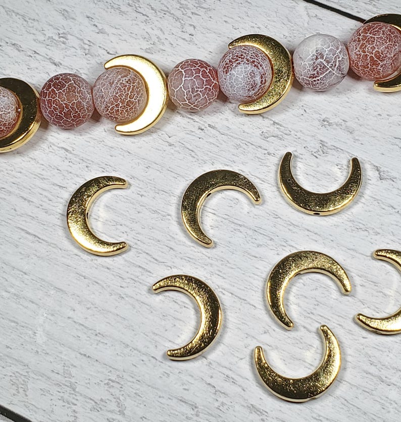 Puede incluir: Componentes para la fabricaci&oacute;n de joyas: abalorios dorados en forma de media luna y una hebra de cuentas redondas estampadas en rojo, rosa y blanco. Las cuentas tienen un patr&oacute;n agrietado en forma de telara&ntilde;a.