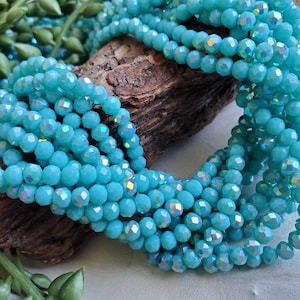 May include: Close-up of strands of light blue faceted beads. The beads have an iridescent sheen and are arranged on a piece of wood. The beads are a vibrant turquoise color and are likely used for jewelry making.