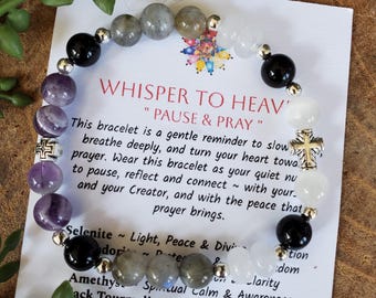 Puede incluir: Un brazalete de cuentas con piedras negras, blancas, grises y moradas. El brazalete está junto a una tarjeta con el texto "WHISPER TO HEAVEN" y "PAUSE & PRAY". La tarjeta también enumera las propiedades de las piedras.