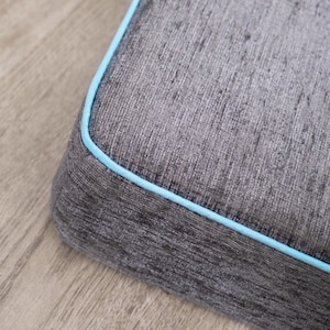 May include: Close-up of a gray cushion with a light blue trim. The cushion has a textured fabric surface.
