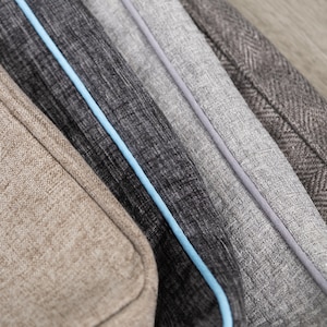 May include: Close-up of four fabric swatches in different colors and textures. The swatches are arranged in a row, with the lightest color at the top and the darkest color at the bottom. The swatches have a subtle herringbone pattern and are trimmed with a light blue piping.