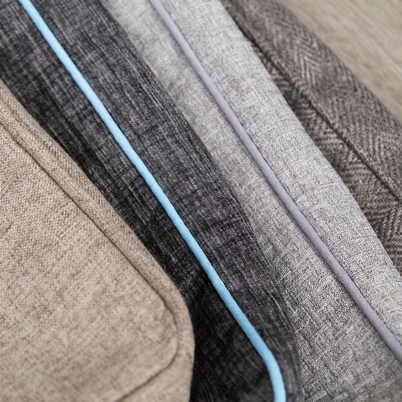 May include: Close-up of four fabric swatches in different colours and textures. The swatches are arranged in a row, with the lightest colour at the top and the darkest colour at the bottom. The swatches have a subtle herringbone pattern and are trimmed with a light blue piping.