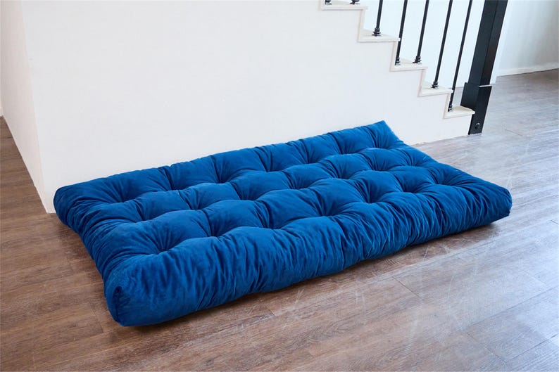 May include: A blue velvet floor cushion with tufted buttons. The cushion is rectangular and has a soft, plush texture.