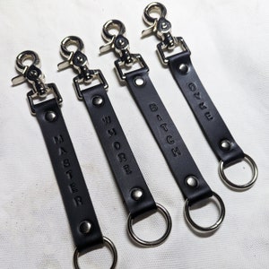 Puede incluir: Cuatro llaveros de cuero negro con anillas y cierres de metal plateado. Cada llavero tiene una palabra diferente impresa en él: "MASTER", "WHORE", "BITCH" y "DYKE".