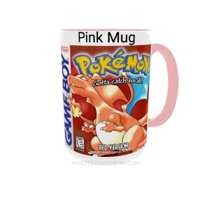 May include: A pink ceramic mug featuring the Pok&eacute;mon Red Version Game Boy game cover art. The design includes the orange Charizard character, the Pok&eacute;mon logo, the text Gotta catch 'em all!, Red Version, and the Game Boy and E rating logos.