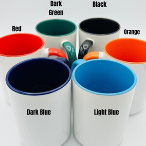 May include: A collection of white ceramic mugs with colored interiors and handles. The interior colors include red, dark green, black, orange, dark blue, and light blue. Each mug has the interior color labeled on the side.