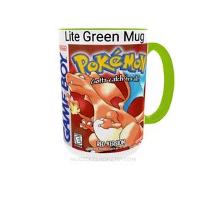 May include: A white ceramic mug with a lime green handle and interior. The exterior features a graphic of the Pokemon Red Version Game Boy game box art, including the Charizard character, the Pokemon logo, and the text Gotta catch 'em all!