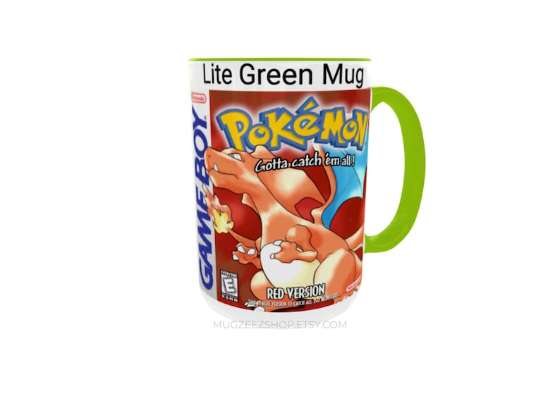 May include: A white ceramic mug with a lime green handle and interior. The exterior features a graphic of the Pokemon Red Version Game Boy game box art, including the Charizard character, the Pokemon logo, and the text Gotta catch 'em all!