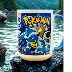 May include: A white ceramic mug with a blue handle featuring a graphic of the Pokemon Blastoise, the Game Boy logo, and the text Pokemon Gotta catch 'em all! Blue Version with an ESRB E rating symbol and the Nintendo logo printed on the front.