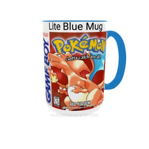 May include: A ceramic mug with a bright blue handle and rim, featuring a graphic print of the Pok&eacute;mon Red Version Game Boy game cover. The design includes the orange Charizard character, the Pok&eacute;mon logo, and the text Gotta catch 'em all!