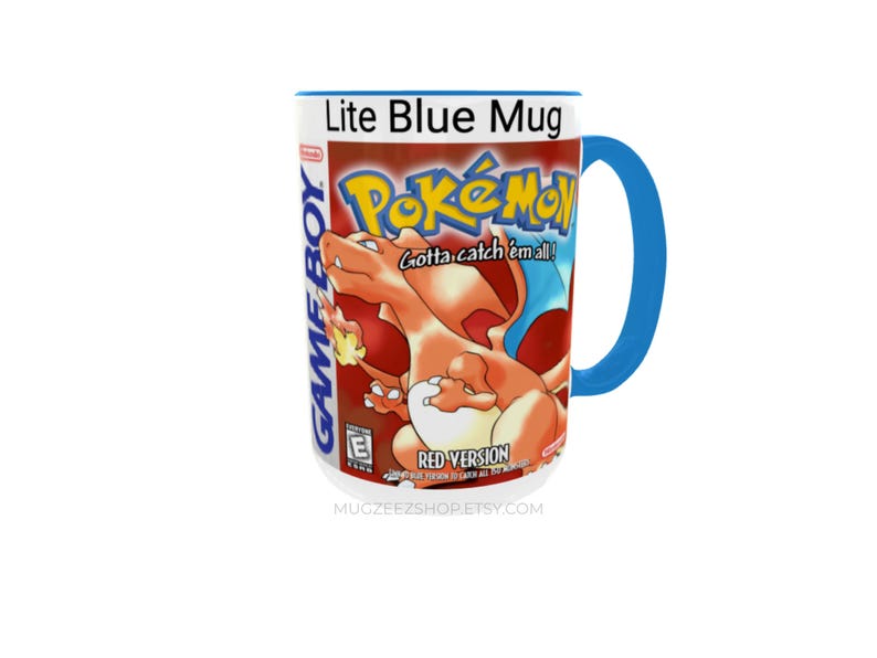 May include: A ceramic mug with a bright blue handle and rim, featuring a graphic print of the Pok&eacute;mon Red Version Game Boy game cover. The design includes the orange Charizard character, the Pok&eacute;mon logo, and the text Gotta catch 'em all!