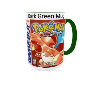May include: A dark green ceramic mug featuring a graphic print of the Pok&eacute;mon Red Version Game Boy game cover. The design includes the orange Charizard character, the Pok&eacute;mon logo, the text Gotta catch 'em all!, and the Game Boy branding.