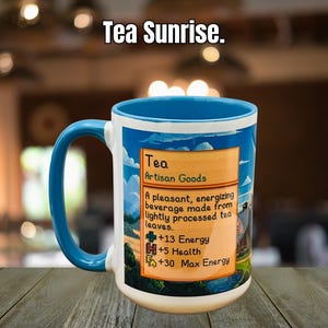 May include: A white ceramic mug with a blue handle and rim, featuring a colorful design with the text "Tea Sunrise." The mug has a label that reads "Tea Artisan Goods" and lists energy and health benefits.