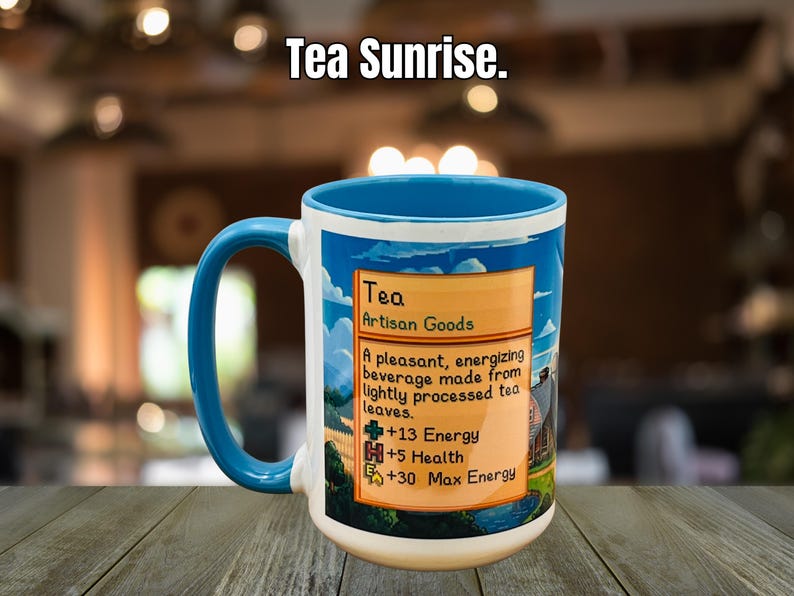 May include: A white ceramic mug with a blue handle and rim, featuring a colorful design with the text "Tea Sunrise." The mug has a label that reads "Tea Artisan Goods" and lists energy and health benefits.