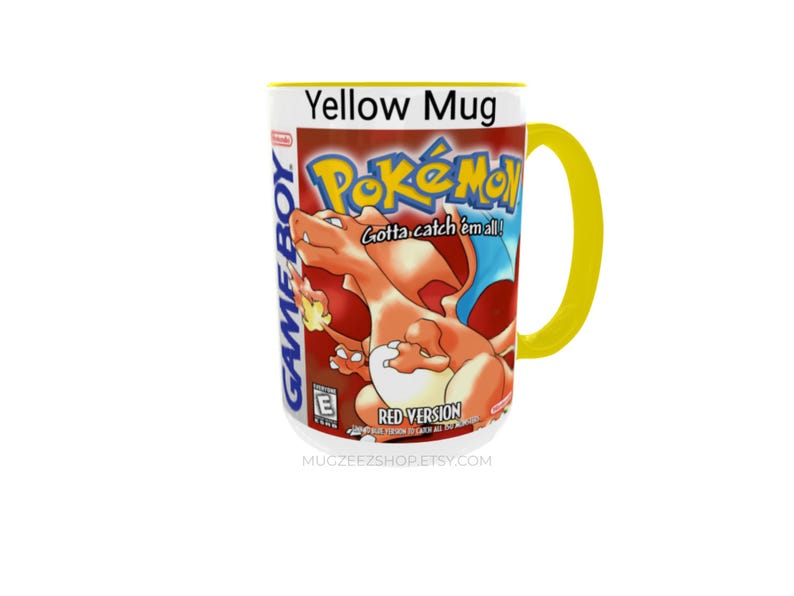 May include: A yellow ceramic mug featuring a graphic print of the Pok&eacute;mon Red Version Game Boy game cover. The design includes the orange Charizard character, the Pok&eacute;mon logo, the text Gotta catch 'em all!, and the Game Boy branding.