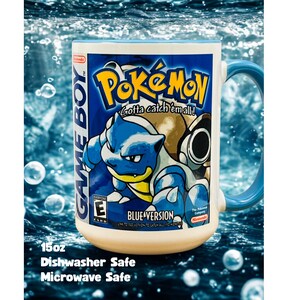 May include: A white ceramic mug with a blue handle featuring a graphic of the Pokemon Blastoise from the Game Boy Blue Version game. The design includes the text Pokemon, Gotta catch 'em all!, Game Boy, and Blue Version. It holds 15oz.