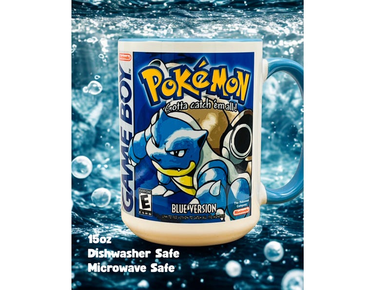 May include: A white ceramic mug with a blue handle featuring a graphic of the Pokemon Blastoise from the Game Boy Blue Version game. The design includes the text Pokemon, Gotta catch 'em all!, Game Boy, and Blue Version. It holds 15oz.