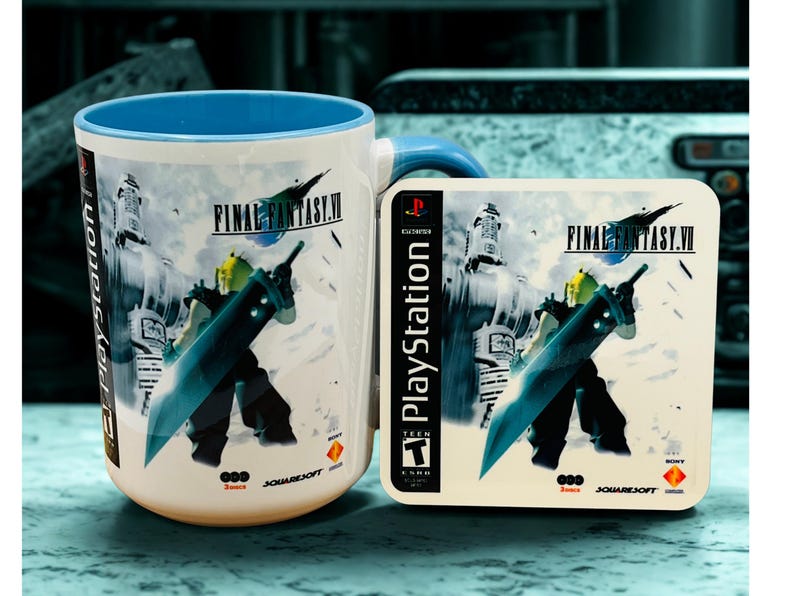 Op de afbeelding: Witte keramische mok en onderzetter set met Final Fantasy VII artwork. De mok heeft een blauwe binnenkant en oor, de onderzetter toont het PlayStation logo en speld details. Het ontwerp toont een personage met een groot zwaard.