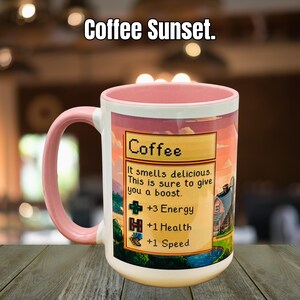 May include: A white coffee mug with a pink handle and rim, featuring a sunset design and the text "Coffee Sunset." The mug has a graphic with the word "Coffee" and text that reads "It smells delicious. This is sure to give you a boost."
