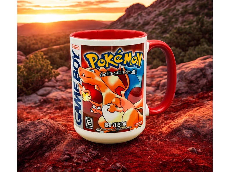 May include: A white ceramic mug with a red interior and handle, featuring a graphic of the Pok&eacute;mon Red Version video game cover art. The design includes the Pok&eacute;mon logo, the text Gotta catch 'em all!, Game Boy branding, and an E rating icon.