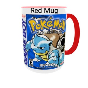 May include: A white ceramic mug with a bright red handle and rim, featuring a graphic print of the Pok&eacute;mon Blue Version Game Boy game cover. The design includes the Pok&eacute;mon logo, the text Gotta catch 'em all!, Blastoise, and the ESRB E rating.