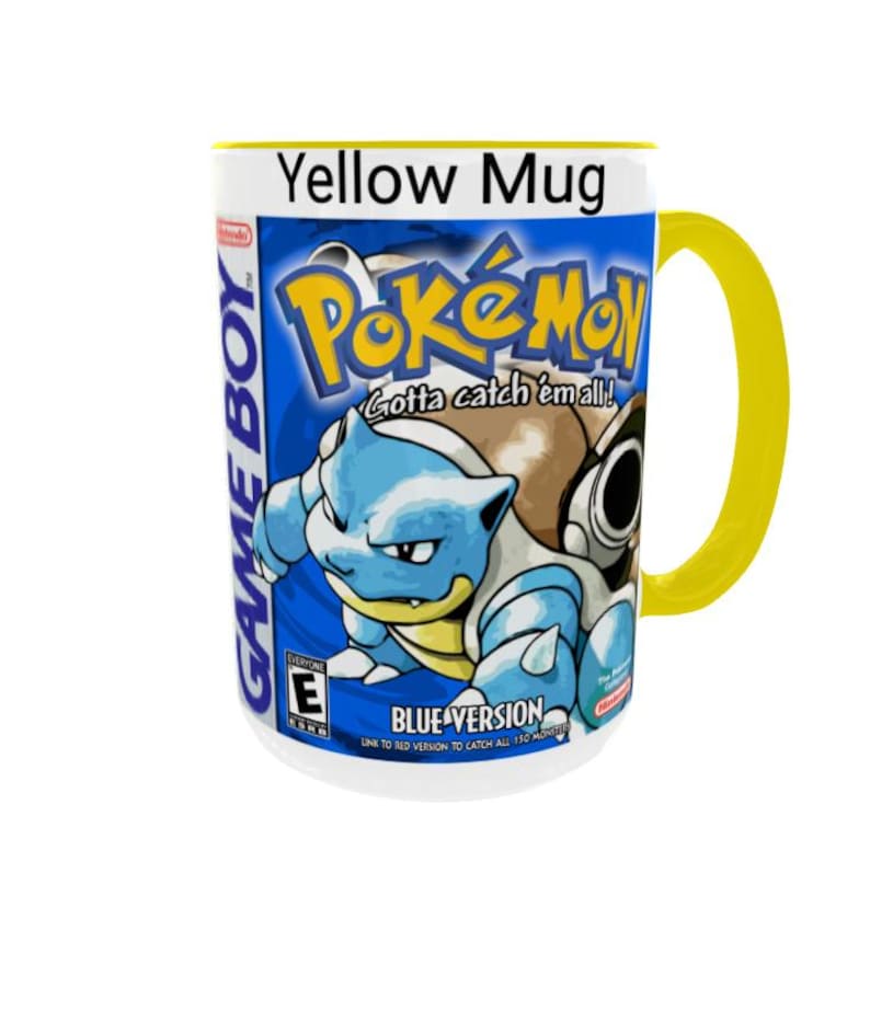 May include: A white ceramic mug with a bright yellow handle and rim. The exterior features a graphic of the Game Boy Pokemon Blue Version video game box art, including the Pokemon Blastoise, the Pokemon logo, and the text Gotta catch em all.