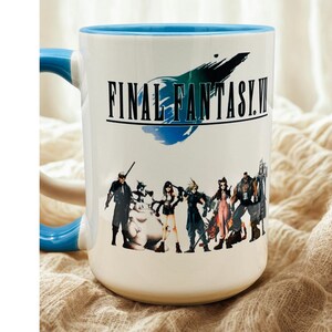 Op de afbeelding: Witte keramische mok met een blauwe binnenkant en handvat. De mok heeft de tekst "FINAL FANTASY VII" met een afbeelding van personages uit de videogame. De mok staat op een beige ondergrond.