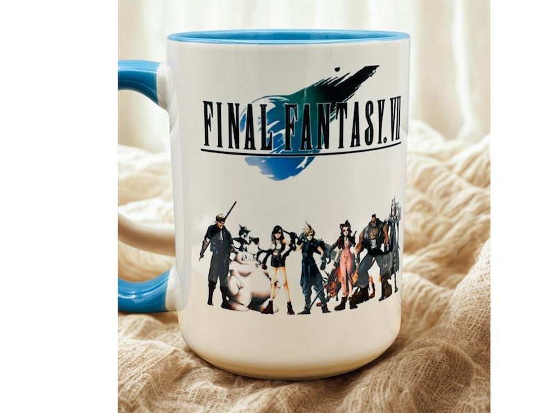 Op de afbeelding: Witte keramische mok met een blauwe binnenkant en handvat. De mok heeft de tekst "FINAL FANTASY VII" met een afbeelding van personages uit de videogame. De mok staat op een beige ondergrond.