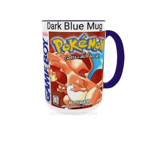 May include: A dark blue ceramic mug featuring a graphic print of the Pokemon Red Version Game Boy game cover. The design includes the orange Charizard character, the Pokemon logo, the text Gotta catch 'em all!, and the Game Boy branding.