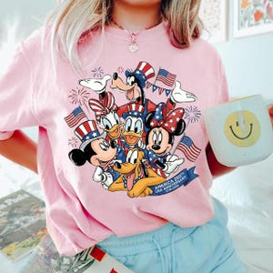 A woman wearing a pink t-shirt with a graphic of Disney characters and a mug with a smiley face.