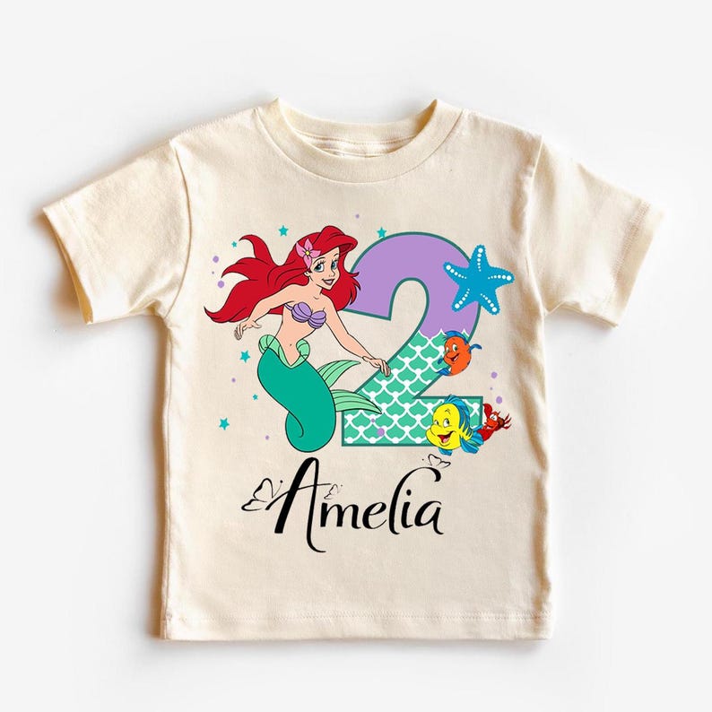 A white t-shirt with a cartoon image of a mermaid character and the name "Amelia" printed on it.