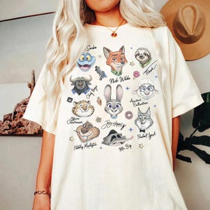 A person wearing a white t-shirt with a graphic design featuring various cartoon animal characters and their names.