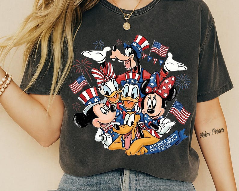 A t-shirt with a graphic design featuring Disney characters such as Minnie Mouse, Donald Duck, Goofy, and Pluto, along with American flags and fireworks.