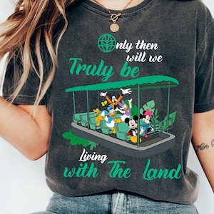 May include: Dark gray t-shirt featuring a graphic of a boat with Disney characters and the text "Only then will we Truly be Living with The land" in green. The boat has a green canopy and is filled with cartoon characters.