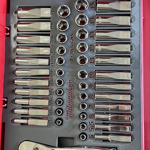 May include: A Milwaukee socket set in a red carrying case. The set includes a range of sockets, a ratchet wrench, and a selection of extension bars. The sockets are arranged in a grid pattern, with the sizes labelled in inches.