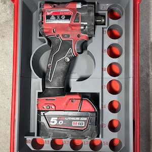 May include: A red and black cordless impact driver and battery in a grey and red tool case with numbered compartments. The battery is a 5.0 Ah RedLithium-Ion M18 battery.