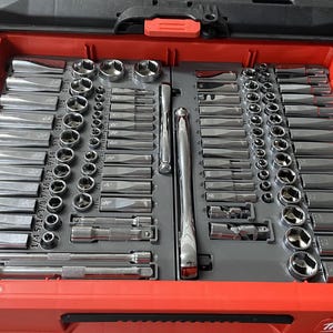 May include: A red toolbox with a grey interior filled with a variety of chrome sockets and spanners. The toolbox has the text "Milwaukee" printed on the front.