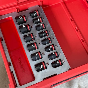 May include: A red toolbox with a grey insert containing black sockets with red bands, numbered from 10 to 27. The open toolbox displays the sockets, ideal for mechanical work. The insert is marked with the text "A+ DESIGNS".